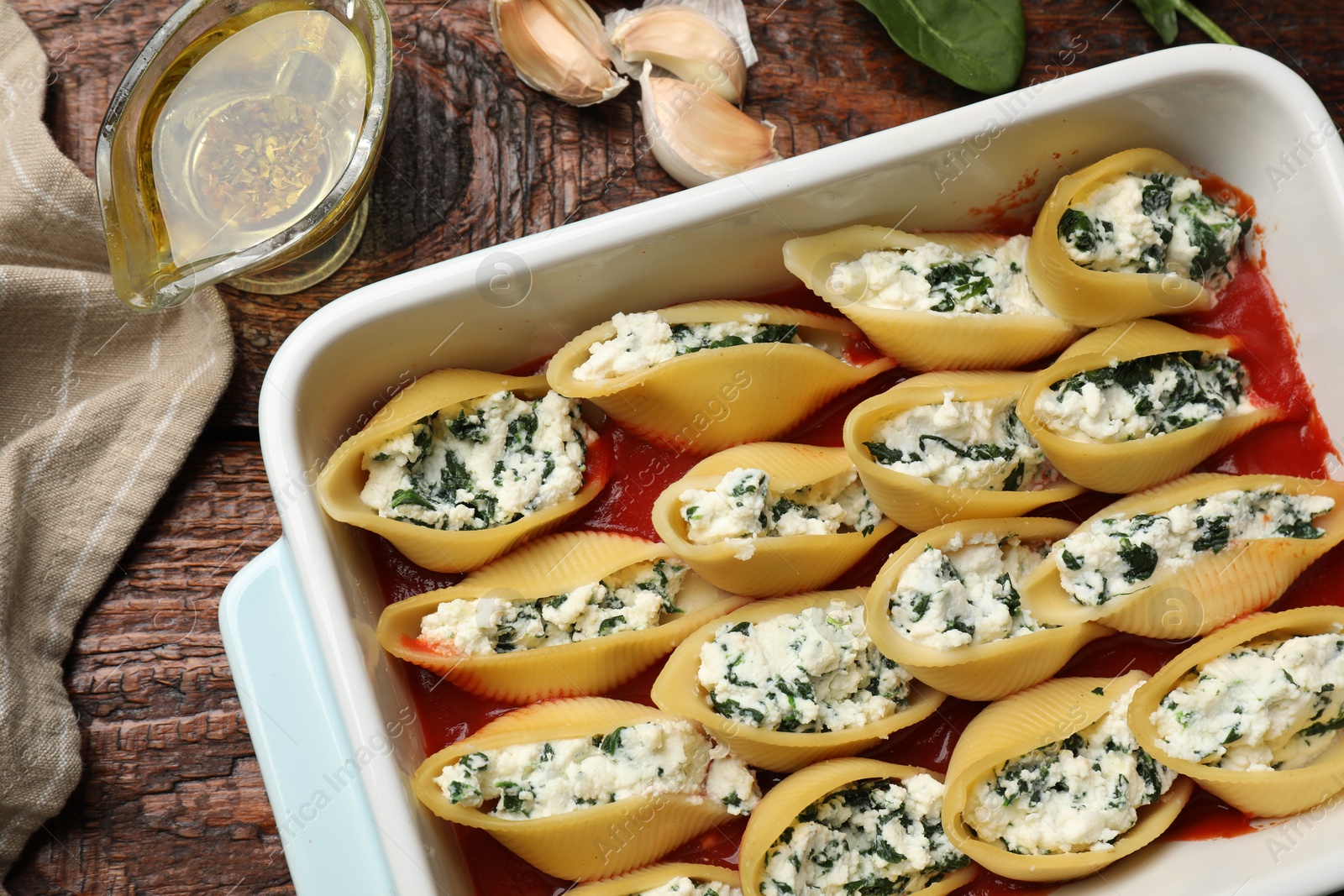 Photo of Delicious conchiglie pasta with ricotta cheese, spinach and tomato sauce in baking dish on wooden table, flat lay