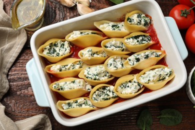 Photo of Delicious conchiglie pasta with ricotta cheese, spinach and tomato sauce in baking dish on wooden table, flat lay