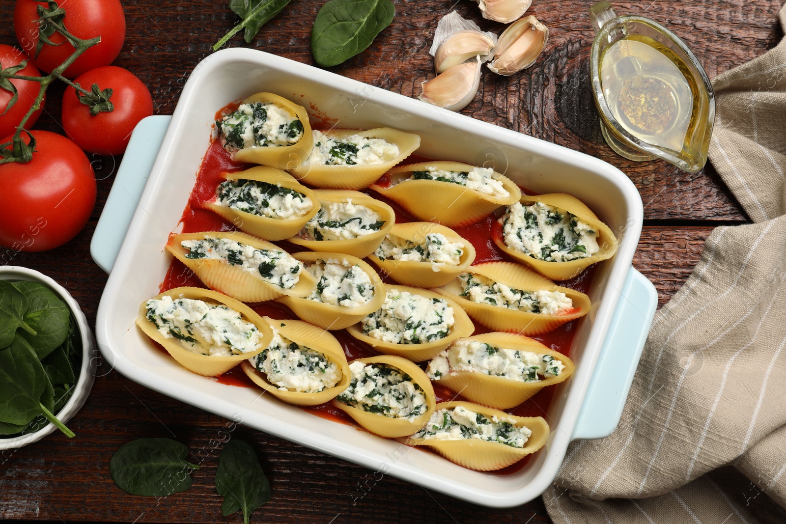 Photo of Delicious conchiglie pasta with ricotta cheese, spinach and tomato sauce in baking dish on wooden table, flat lay