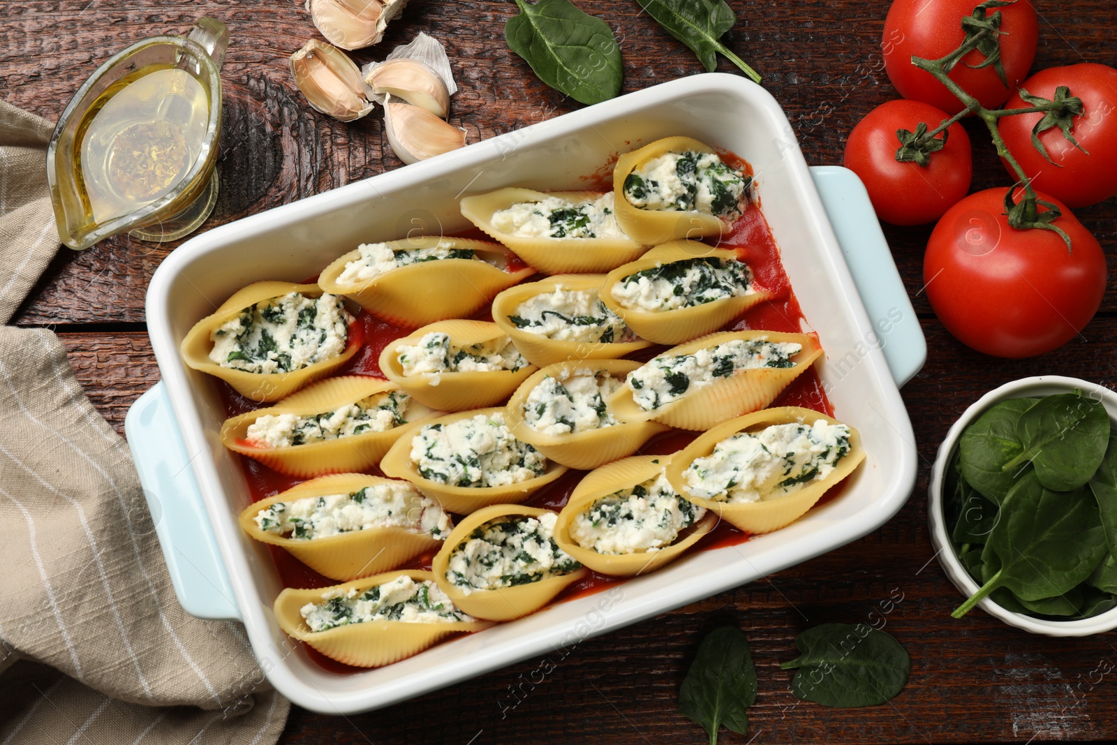 Photo of Delicious conchiglie pasta with ricotta cheese, spinach and tomato sauce in baking dish on wooden table, flat lay