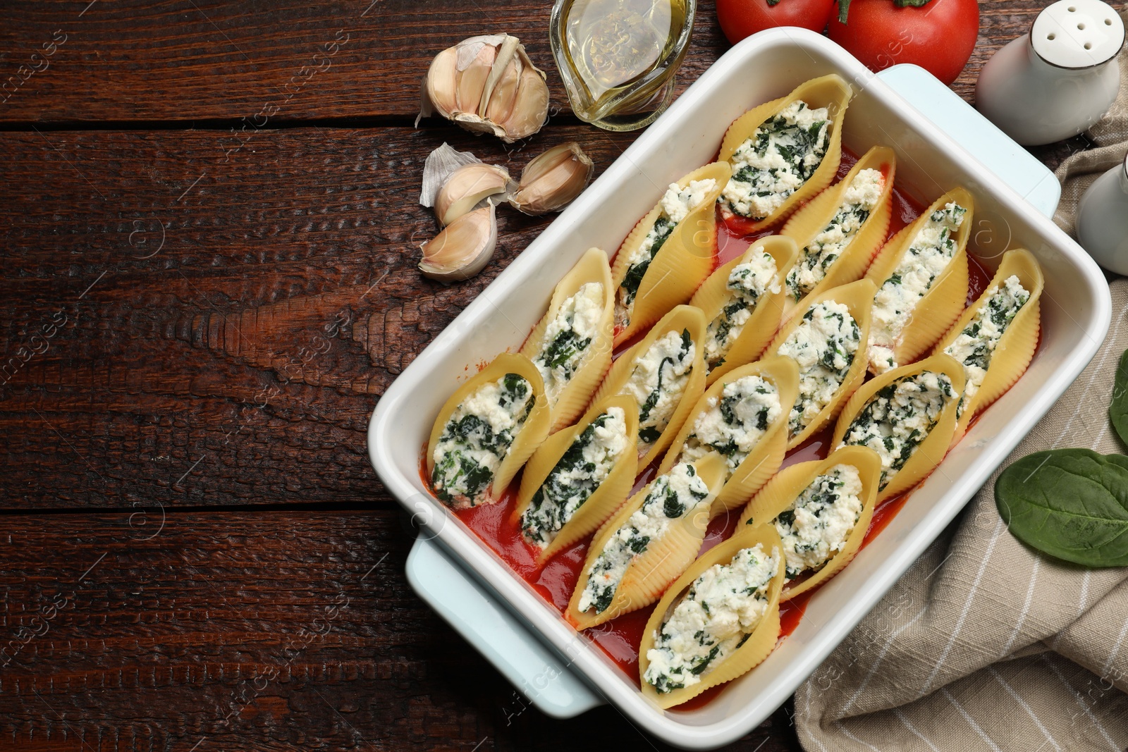 Photo of Delicious conchiglie pasta with ricotta cheese, spinach and tomato sauce in baking dish on wooden table, flat lay. Space for text