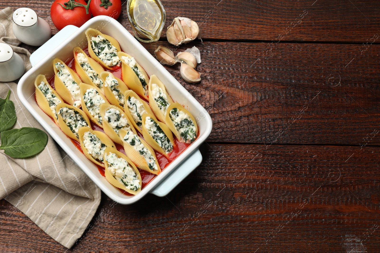 Photo of Delicious conchiglie pasta with ricotta cheese, spinach and tomato sauce in baking dish on wooden table, flat lay. Space for text