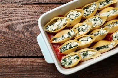 Photo of Delicious conchiglie pasta with ricotta cheese, spinach and tomato sauce in baking dish on wooden table, top view. Space for text