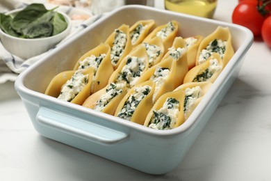 Photo of Delicious conchiglie pasta with ricotta cheese and spinach in baking dish on white marble table, closeup