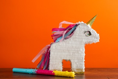 Photo of Bright pinata in shape of unicorn and stick on table against orange background