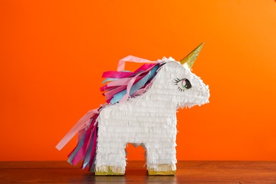 Photo of Bright pinata in shape of unicorn on table against orange background