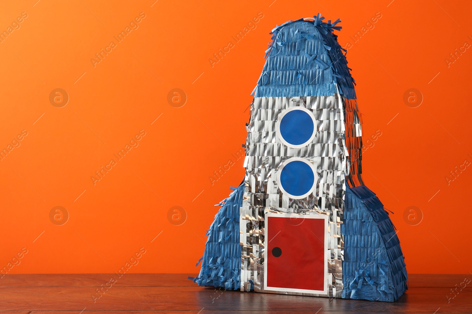 Photo of Bright pinata in shape of spaceship on table against orange background. Space for text