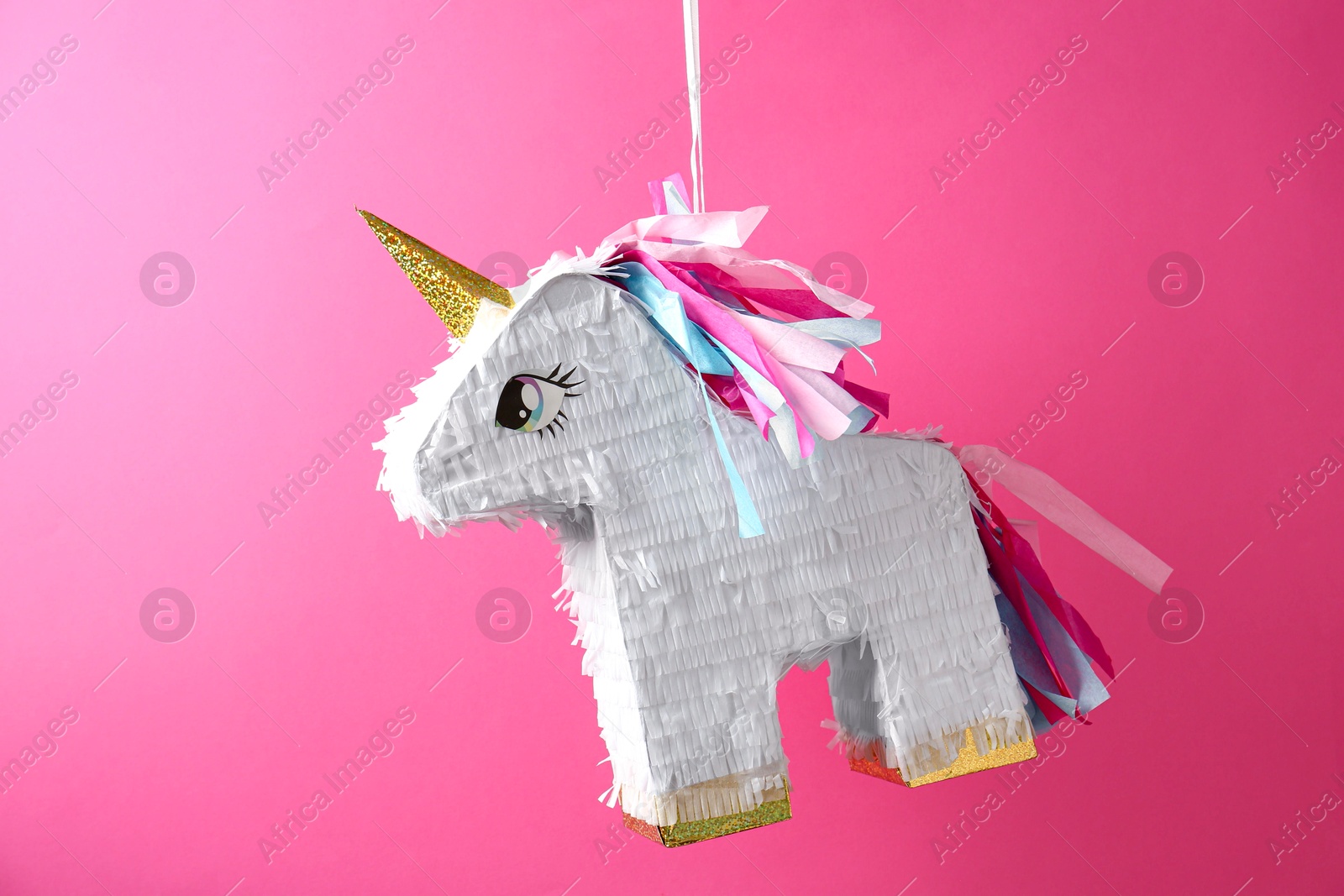 Photo of Bright pinata in shape of unicorn hanging on pink background