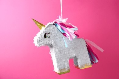 Photo of Bright pinata in shape of unicorn hanging on pink background