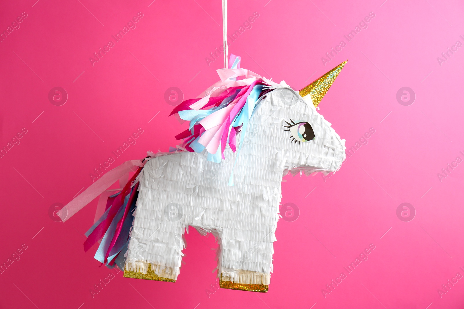 Photo of Bright pinata in shape of unicorn hanging on pink background