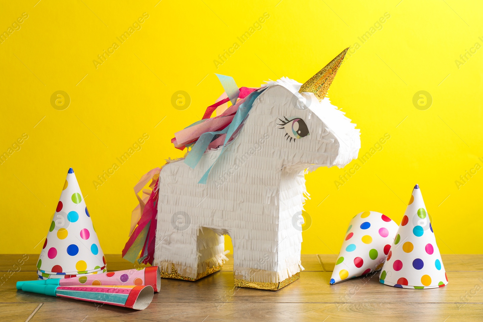 Photo of Beautiful pinata in shape of unicorn, party cones and poppers on wooden table against yellow background