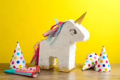 Photo of Beautiful pinata in shape of unicorn, party cones and poppers on wooden table against yellow background