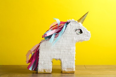 Photo of Beautiful pinata in shape of unicorn on wooden table against yellow background