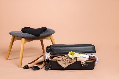 Photo of Suitcase with messy clothes, shoes and stool on beige background