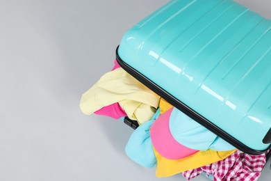 Photo of Packed suitcase full of clothes on light grey background, closeup. Space for text