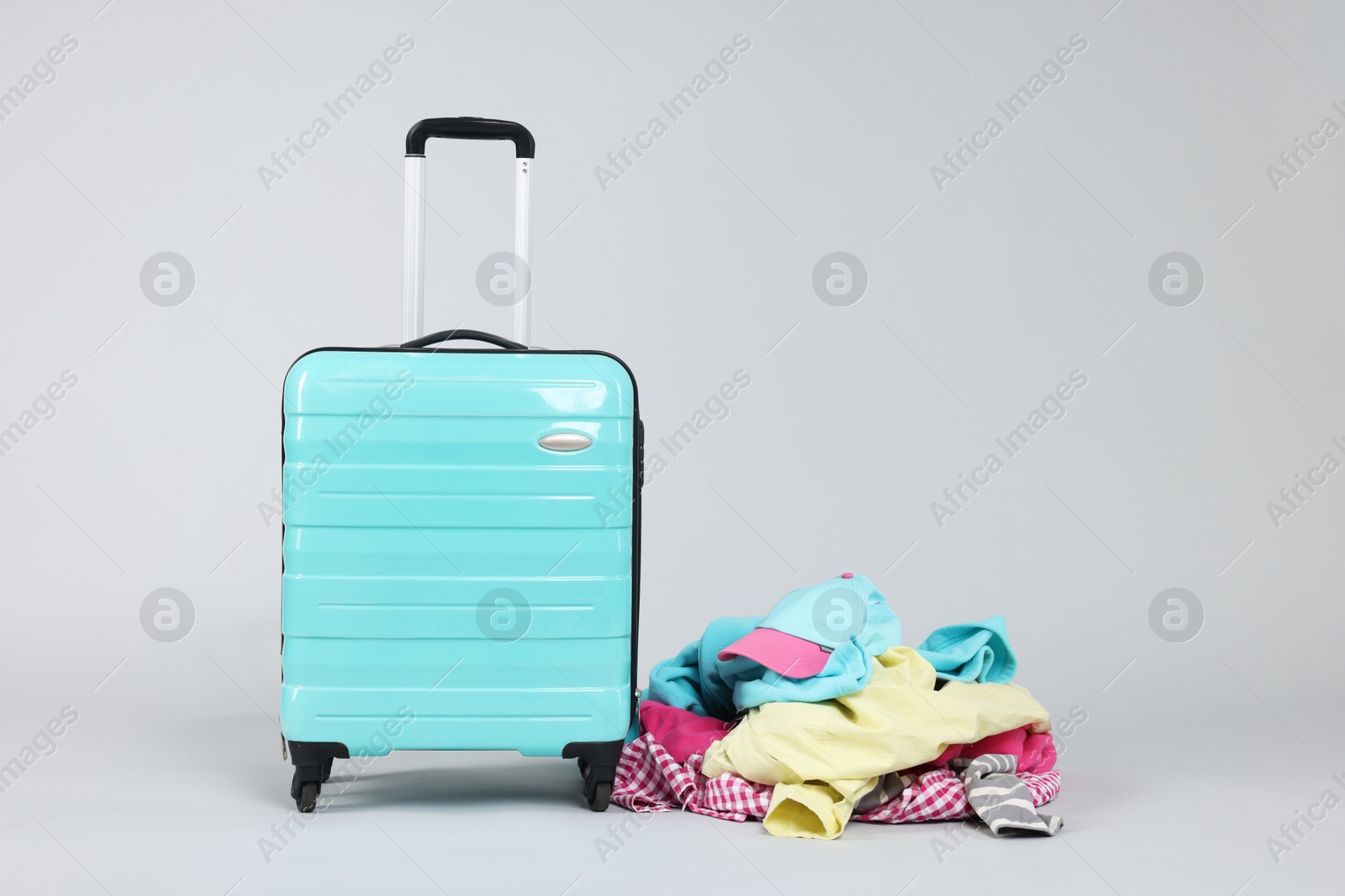 Photo of Suitcase and messy pile of clothes on light grey background. Space for text