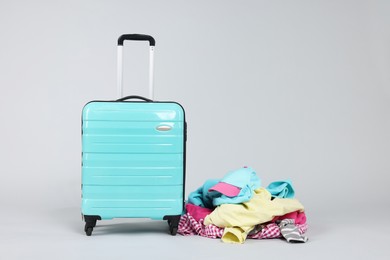 Photo of Suitcase and messy pile of clothes on light grey background. Space for text