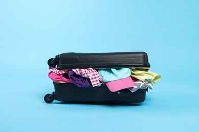 Photo of Packed suitcase full of clothes on light blue background