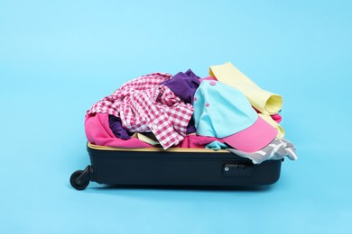 Photo of Packed suitcase full of clothes on light blue background