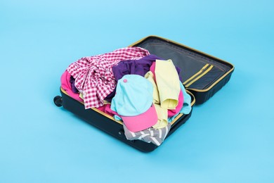 Photo of Packed suitcase full of clothes on light blue background