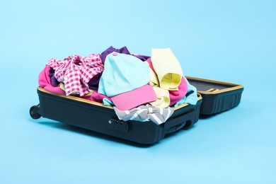 Photo of Packed suitcase full of clothes on light blue background
