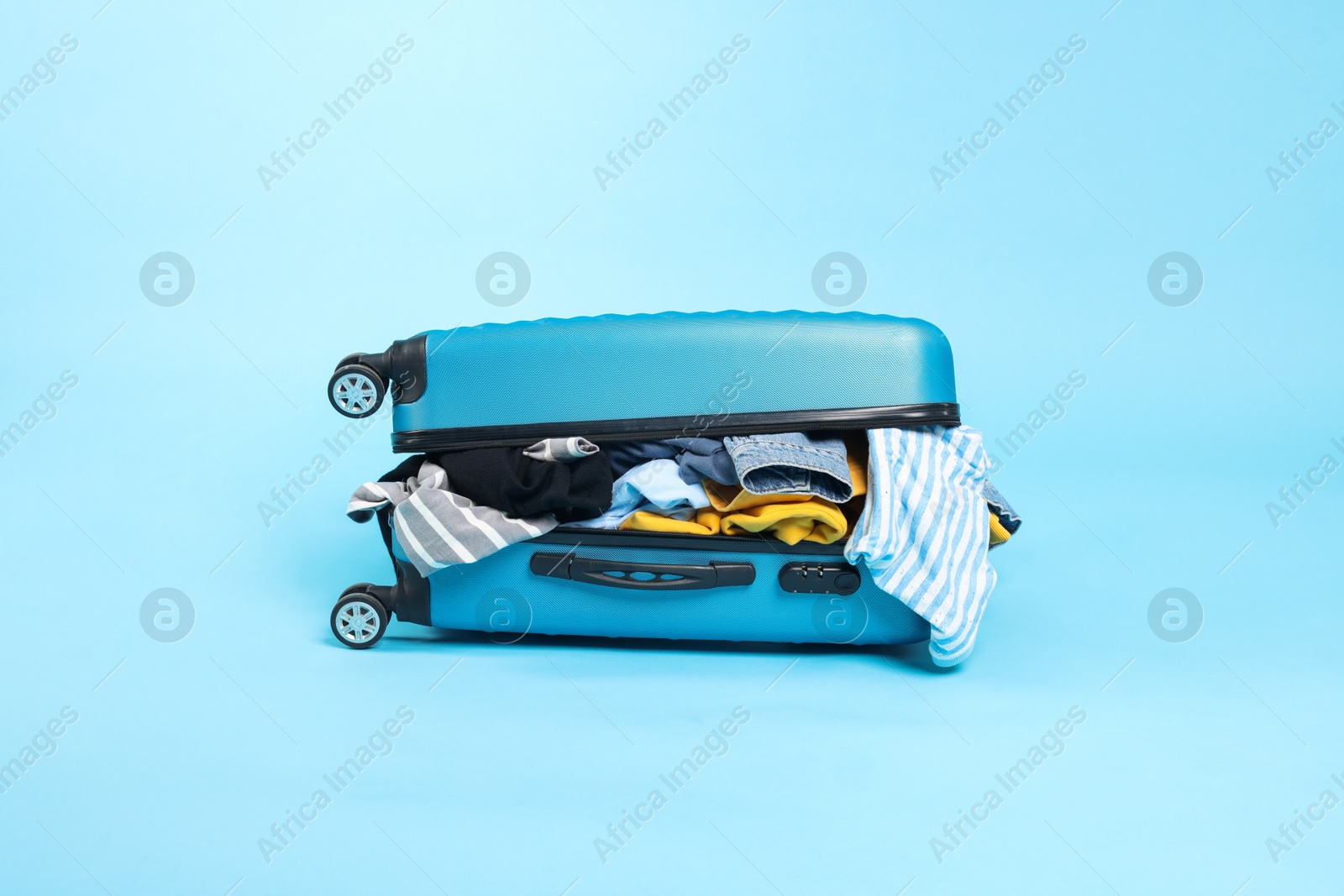 Photo of Packed suitcase full of clothes on light blue background