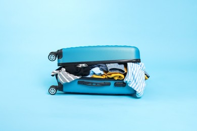 Photo of Packed suitcase full of clothes on light blue background