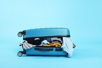 Photo of Packed suitcase full of clothes on light blue background