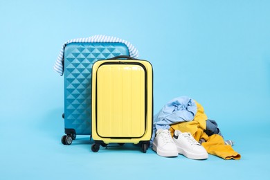 Photo of Suitcases, shoes and messy pile of clothes on light blue background