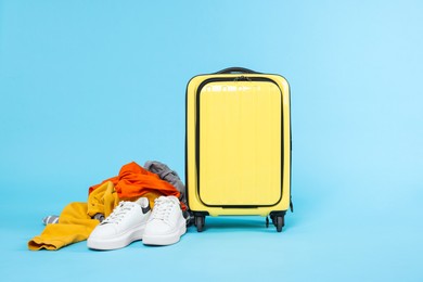 Photo of Suitcase, shoes and messy pile of clothes on light blue background