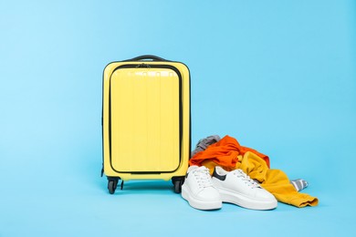 Photo of Suitcase, shoes and messy pile of clothes on light blue background