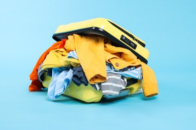 Photo of Packed suitcase full of clothes on light blue background