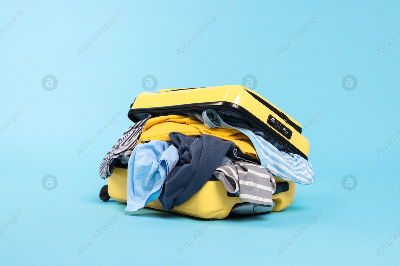Photo of Packed suitcase full of clothes on light blue background