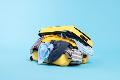 Photo of Packed suitcase full of clothes on light blue background
