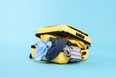 Photo of Packed suitcase full of clothes on light blue background