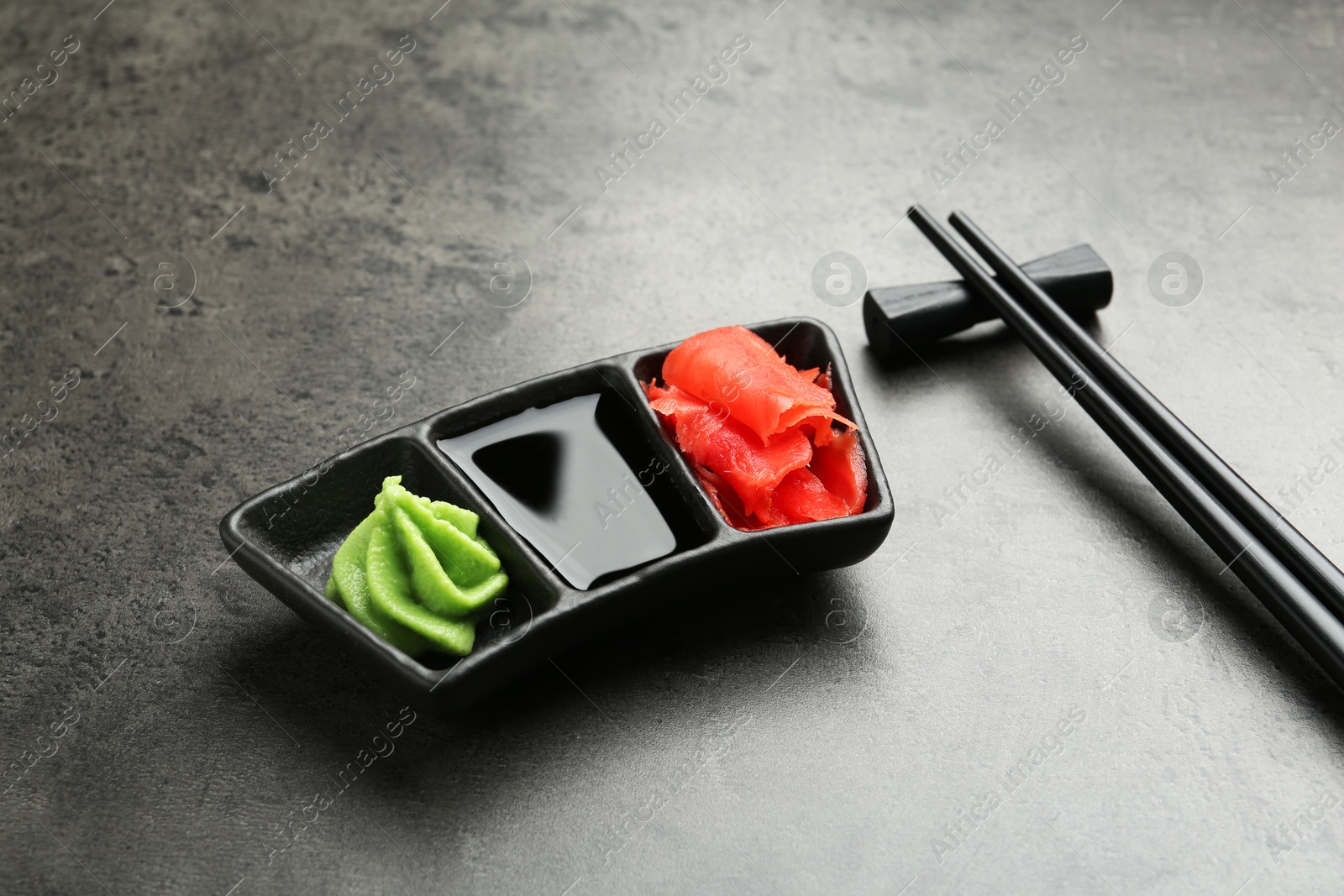 Photo of Hot wasabi paste, soy sauce, ginger and chopsticks on grey textured table, closeup