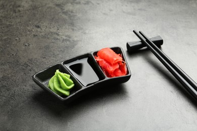 Photo of Hot wasabi paste, soy sauce, ginger and chopsticks on grey textured table, closeup