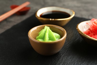 Photo of Hot wasabi paste, soy sauce and ginger on dark table, closeup