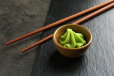 Photo of Hot wasabi paste in bowl and chopsticks on grey textured table, closeup