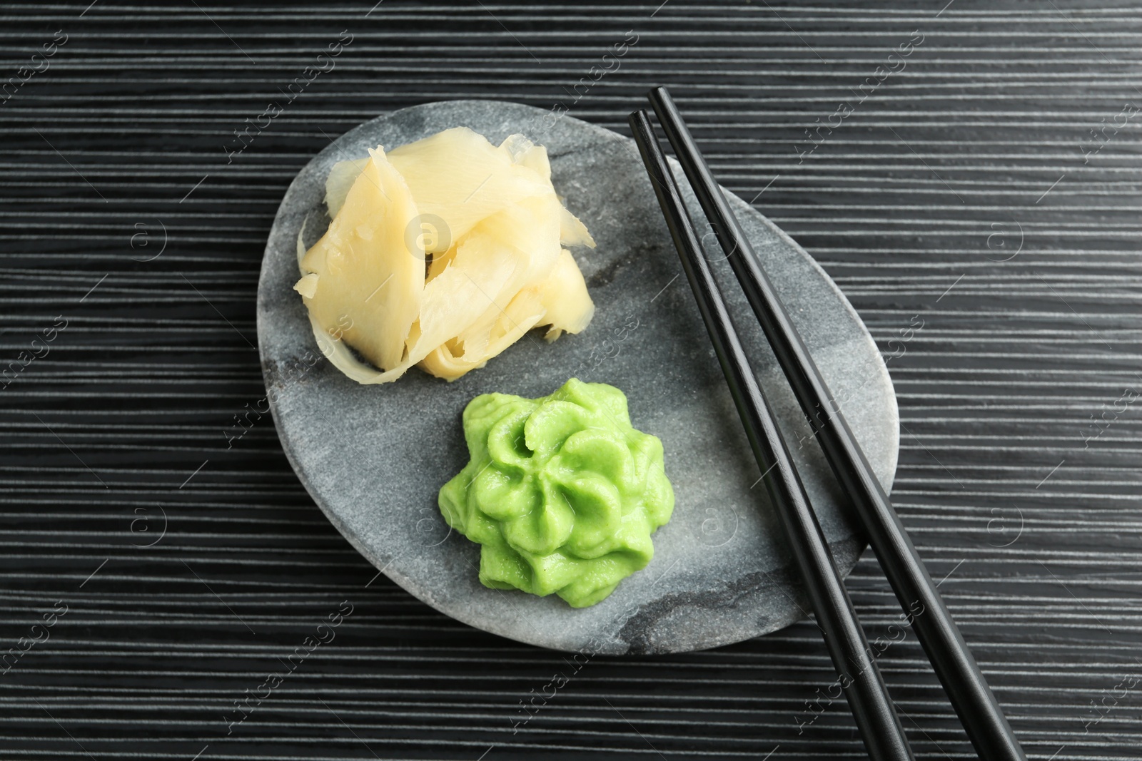 Photo of Hot wasabi paste, ginger and chopsticks on black textured table, top view