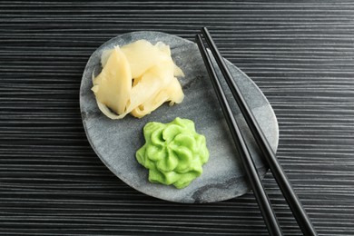 Photo of Hot wasabi paste, ginger and chopsticks on black textured table, top view