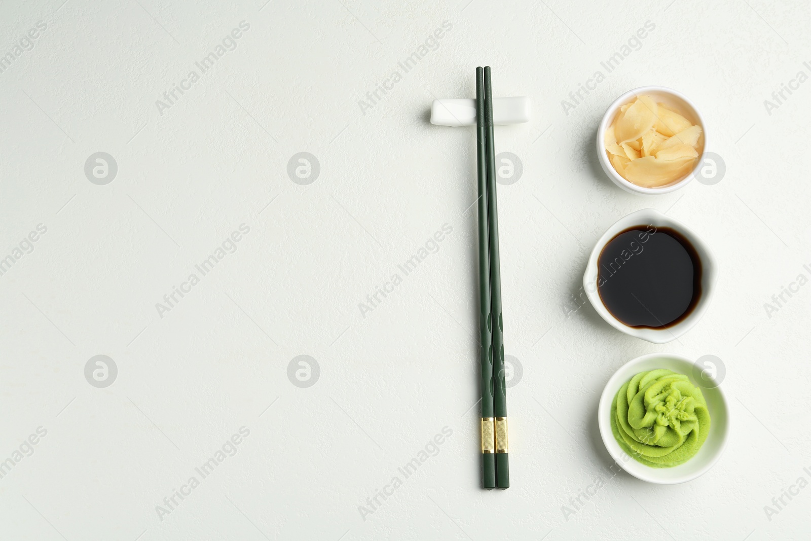 Photo of Hot wasabi paste, soy sauce, ginger and chopsticks on light textured table, flat lay. Space for text