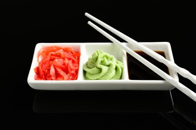 Photo of Hot wasabi paste, soy sauce, ginger and chopsticks on black mirror surface, closeup