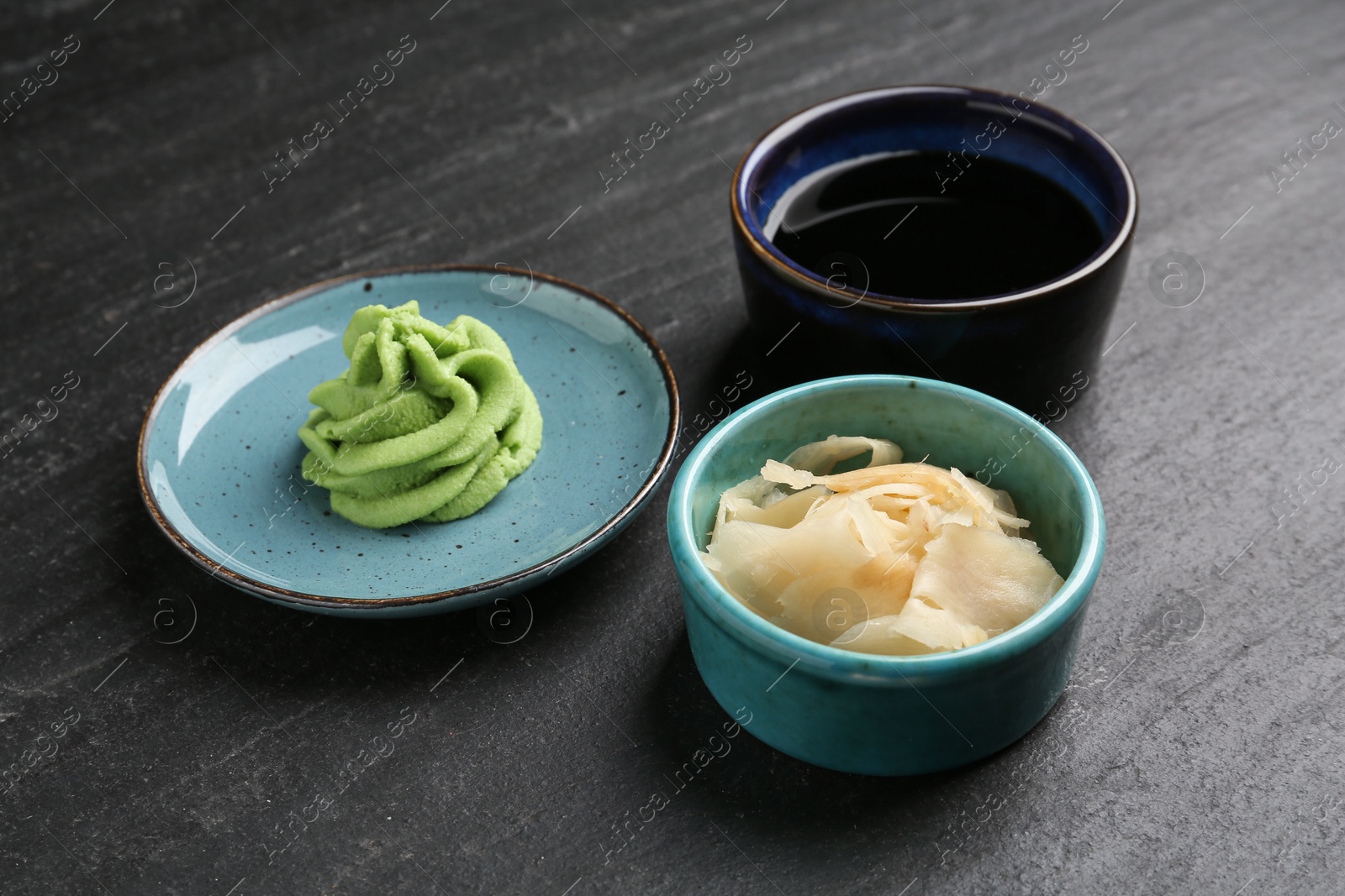 Photo of Hot wasabi paste, soy sauce and ginger on dark textured table, closeup