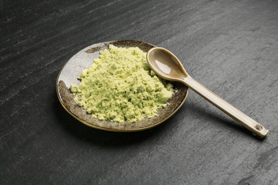 Photo of Plate with dry wasabi powder and spoon on dark textured table, closeup