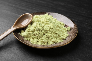 Photo of Plate with dry wasabi powder and spoon on dark textured table, closeup