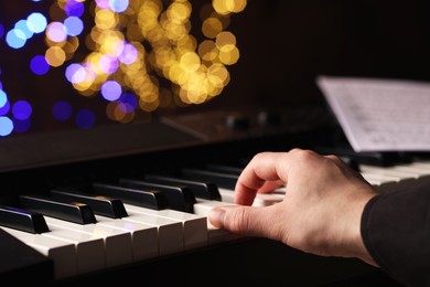 Photo of Man playing piano against blurred lights, closeup. Bokeh effect