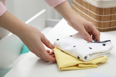 Photo of Woman folding baby clothes at home, closeup