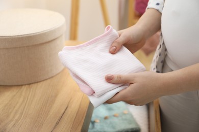 Photo of Pregnant woman with baby clothes at home, closeup