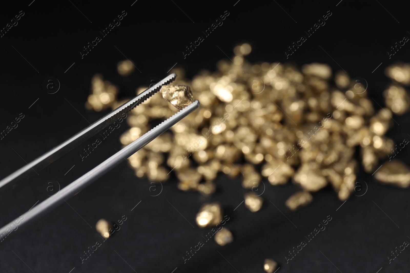 Photo of Tweezers with gold nugget against blurred background, closeup. Space for text